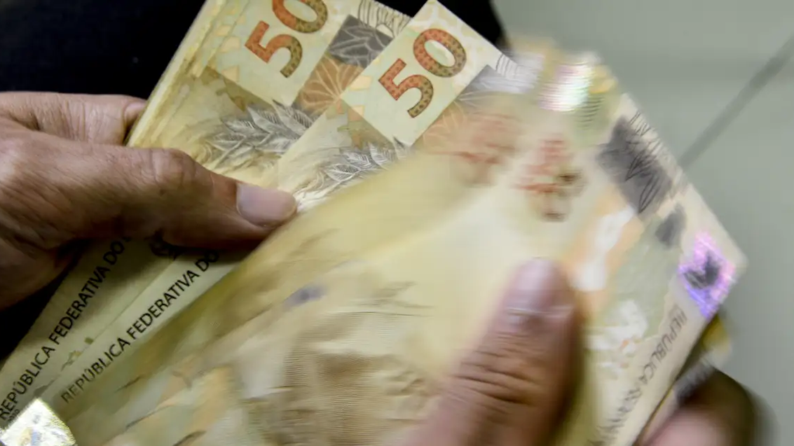 Mãos contam notas de 50 reais