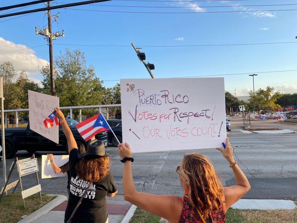 personas con carteles y banderas de puerto rico. Las cartulinas dicen "puerto rico vota por respeto" y "nuestros votos cuentan". 