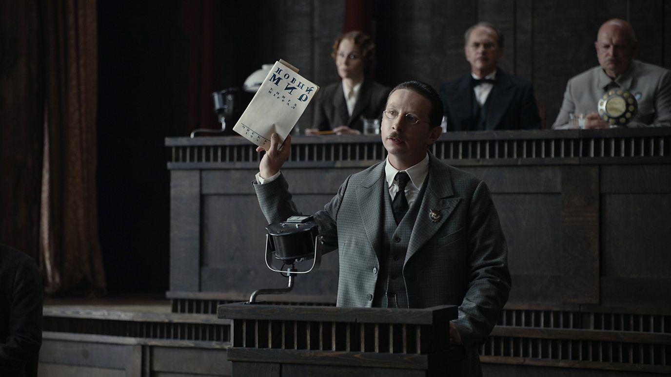 Un hombre muestra un escrito en un estrado, en una escena de la película. 