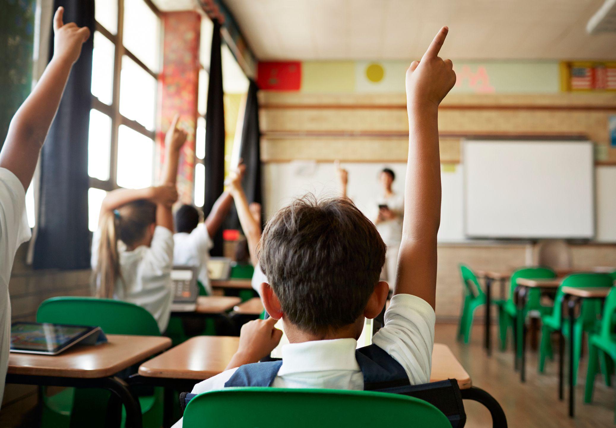 A boy in a classroom with his hand in the air