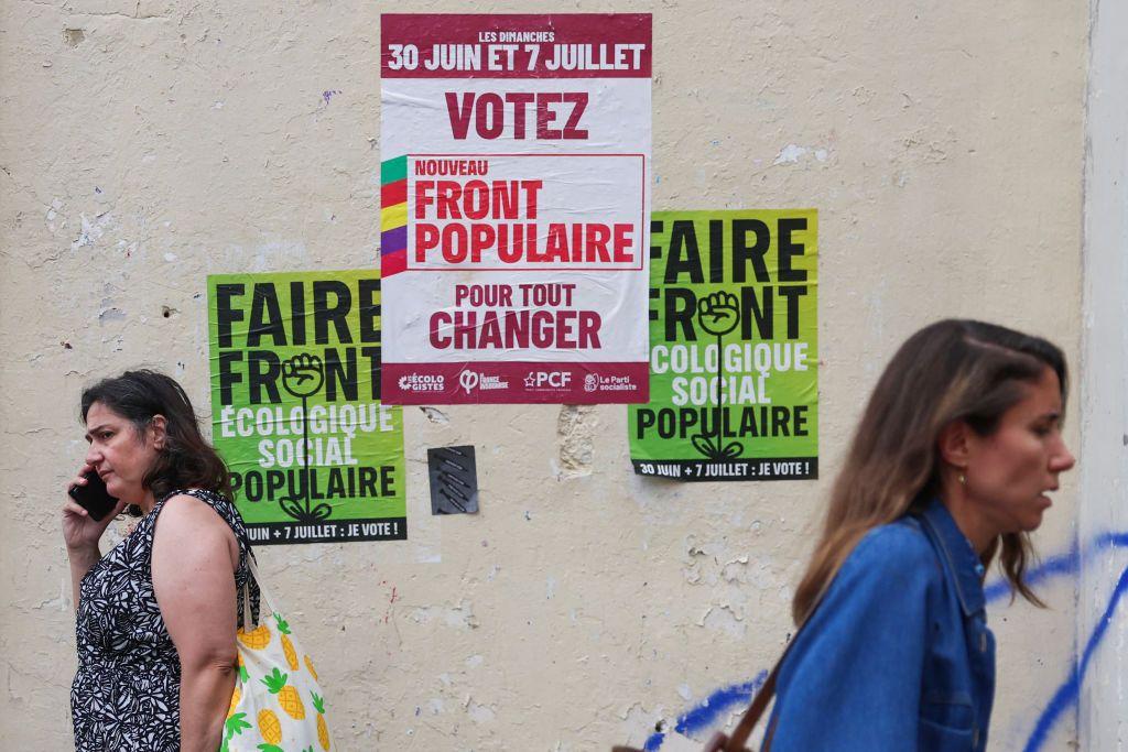اثنان من المارة أمام ملصقات انتخابية للحزب اليساري "الجبهة الشعبية الجديدة" في باريس، في 3 يوليو/تموز 2024، قبل الجولة الثانية من الانتخابات التشريعية في فرنسا