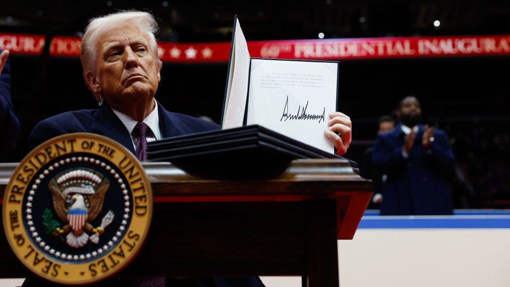 Presiden Donald Trump mengangkat perintah eksekutif yang sudah ditandatanganinya di Capital One Arena, Washington DC, Senin (20/01).