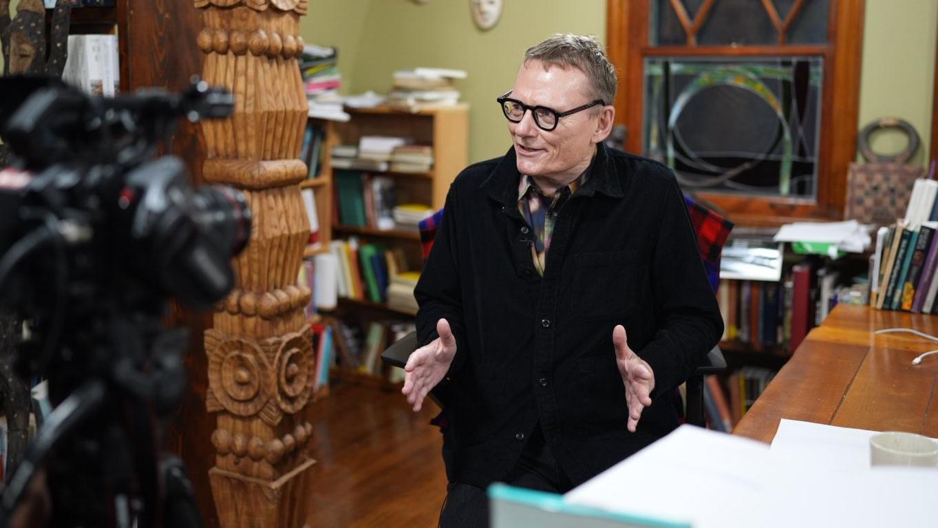 James A. Robinson na frente de uma câmera dentro de um escritório.