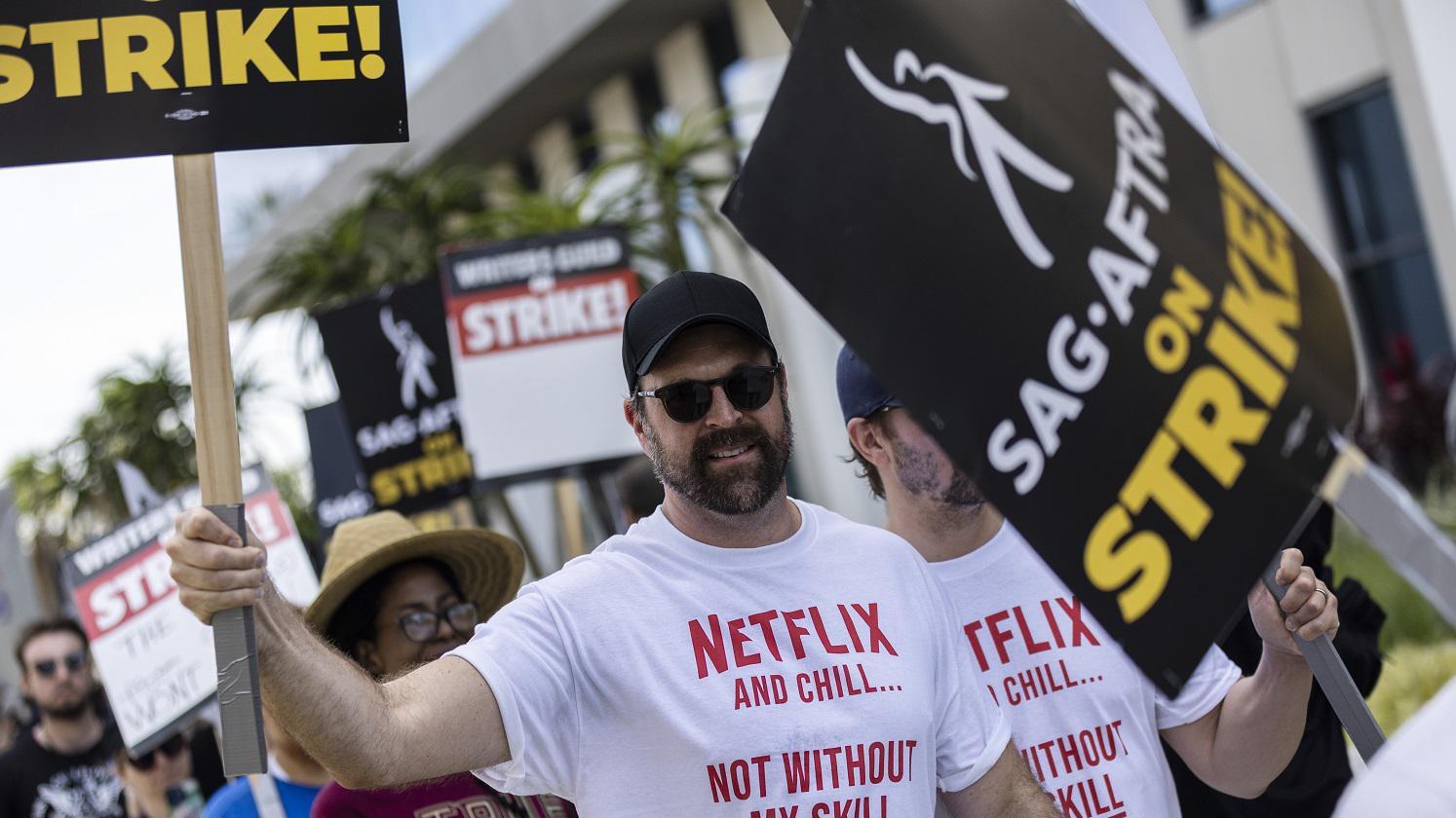 Pessoas protestando e levantando cartazes; na camisa, há menção (e críticas) à Netflix
