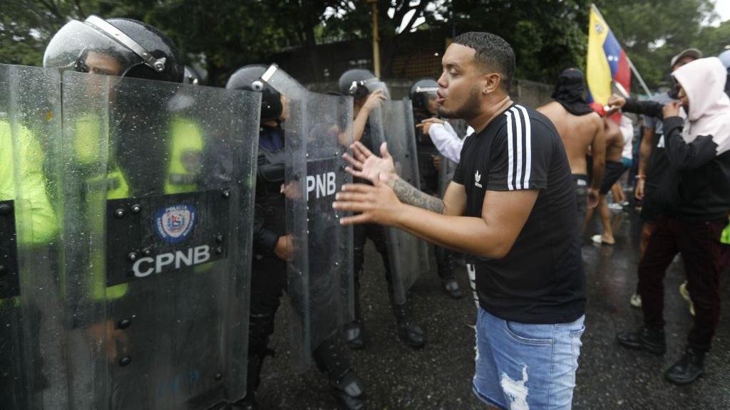 Manifestante tenta dialogar com policiais venezuelanos protegidos por escudos