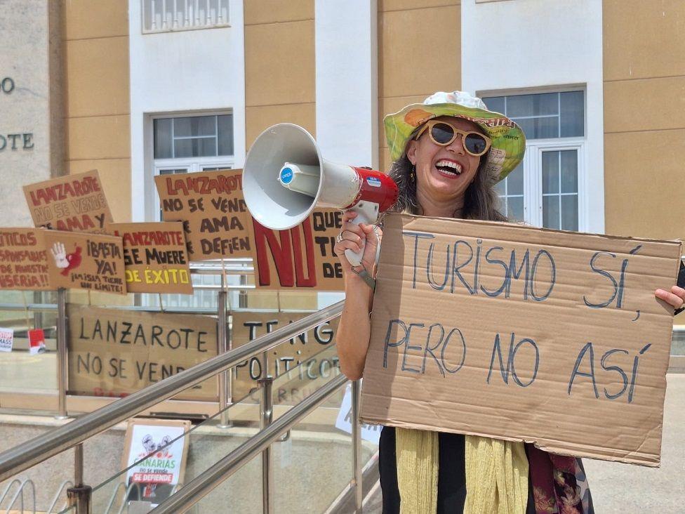 Manifestante con un altoparlante y una pancarta que dice: Turismo sí, pero no así