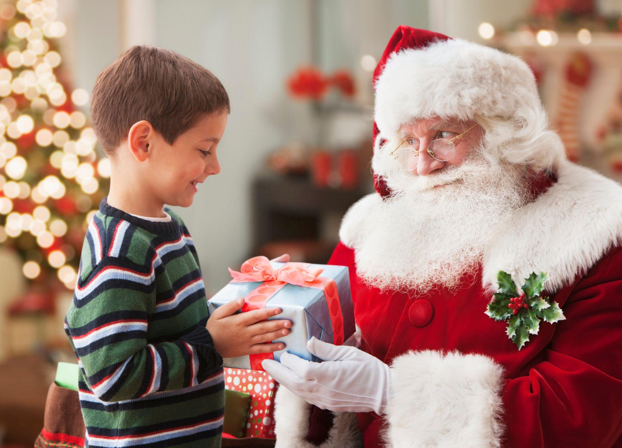 Menino recebendo presente de homem vestido de Papai Noel com decorações de Natal ao fundo