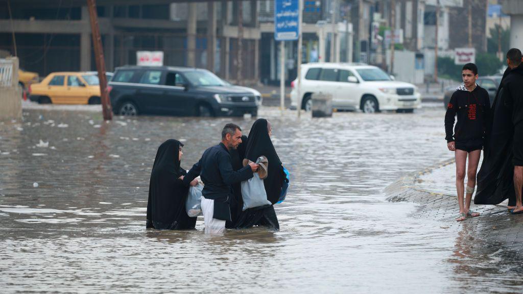 Pessoas caminham pelas ruas inundadas devido à infraestrutura precária após fortes chuvas em Najaf, Iraque, 26 de março de 2023