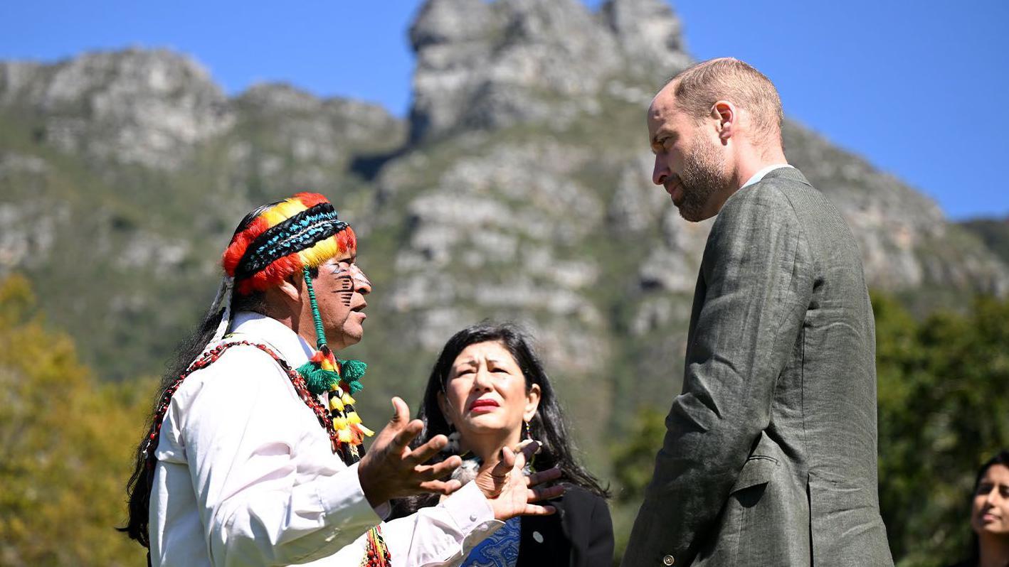 Príncipe William  conversa com duas pessoas, ao fundo a table mountain