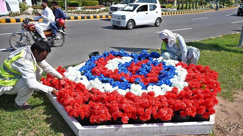 Two men are placing artificial flowers' bed on the roadside in Islamabad as preparations are done to host SCO Summit.