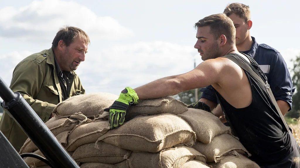 Foto de homens empilhando sacas no que parece ser uma barricada. 