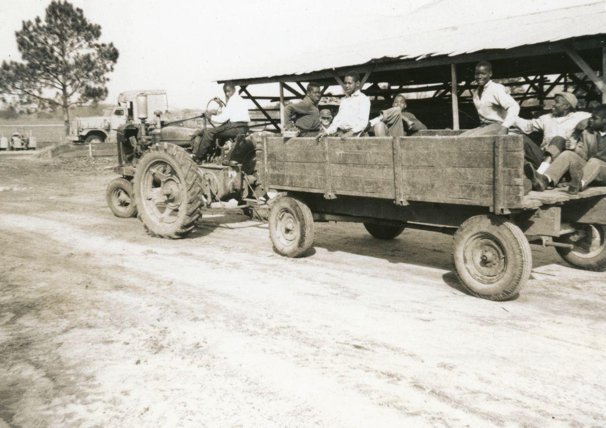 Una vieja foto del reformatorio, en el que un chico está manejando un tractor y un grupo de niños viaja en la carreta que el camión arrastra. 