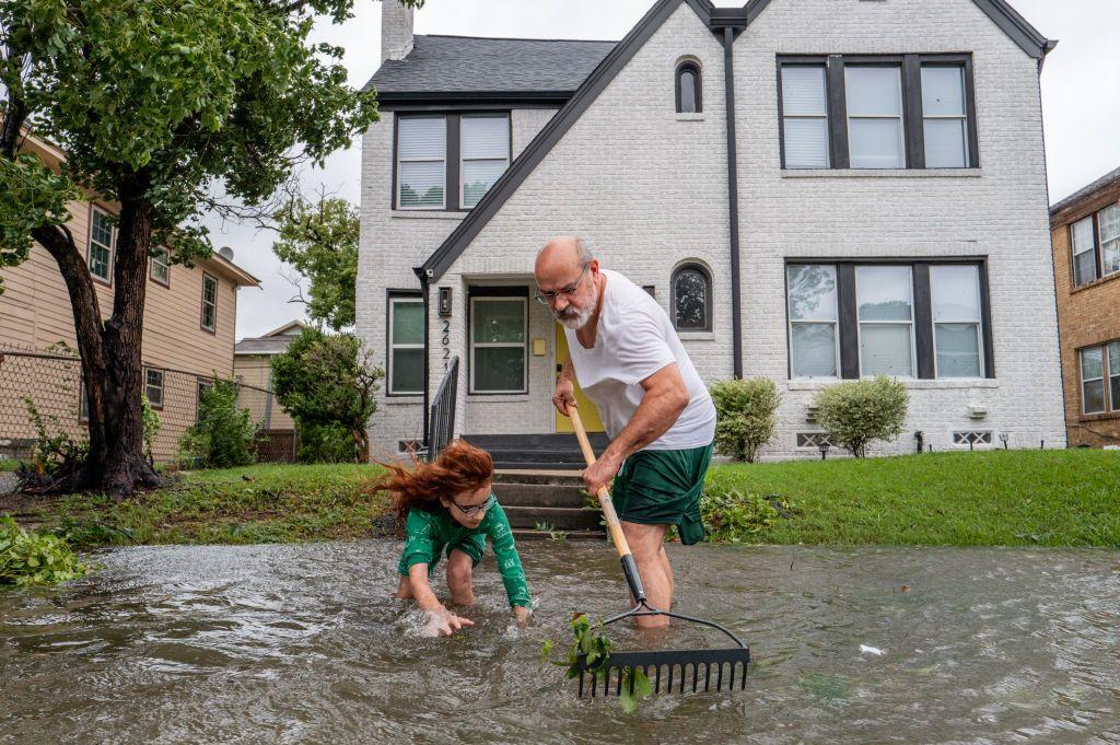 un hombre y una niña limpian un área levemente inundada frente a una casa