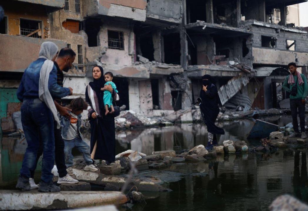 غزيون يقفون قرب مباني دمرتها غارة إسرائيلية في خان يونس