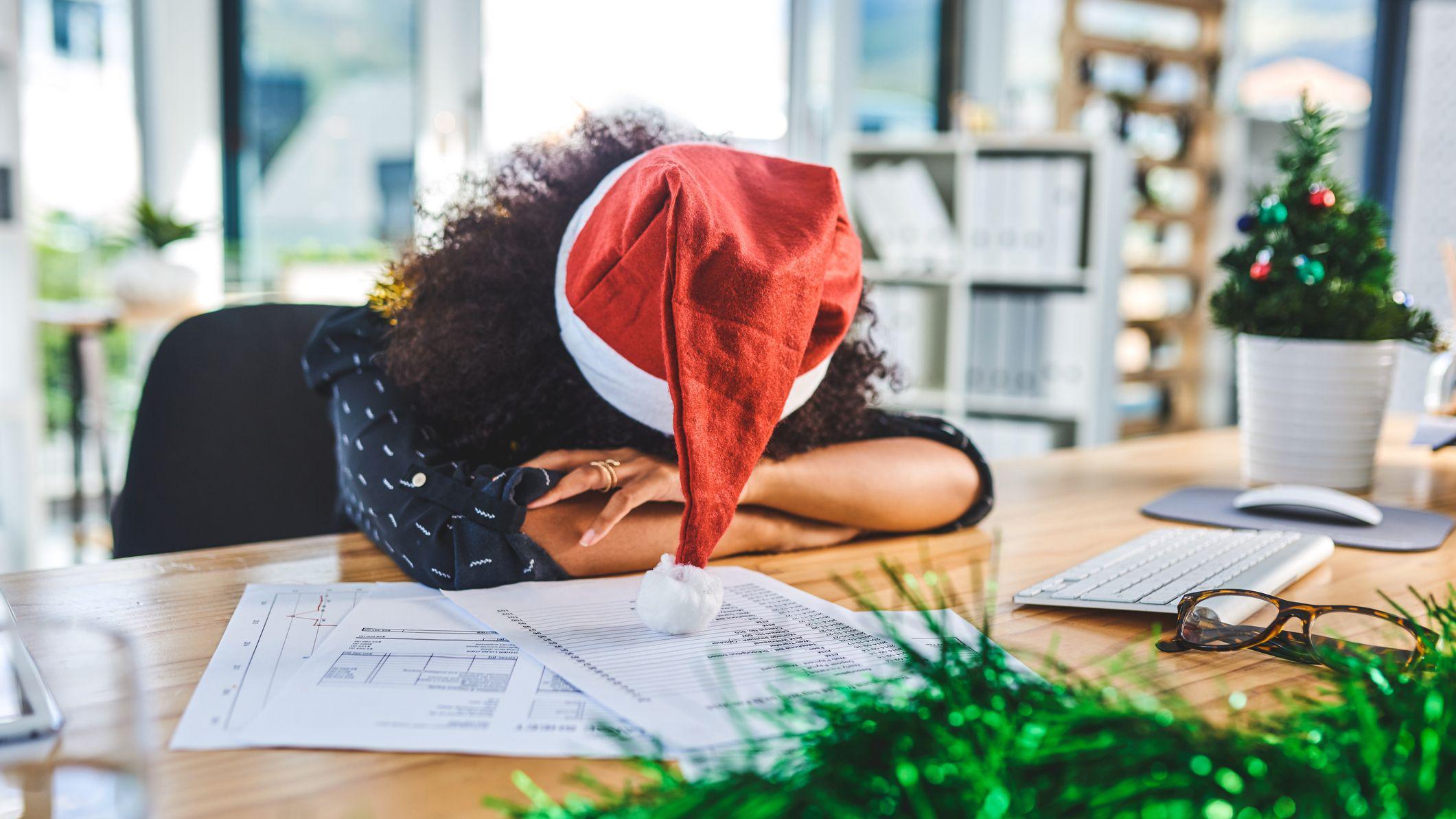 mulher com chapeu de papai noel descansa a cabeça em mesa de escritório