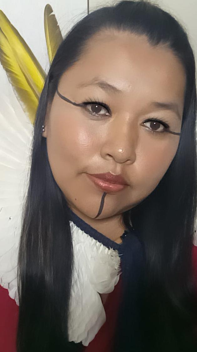 Selfie de Moni Terena; ela aparece com ornamentos de penas e pinturas no rosto