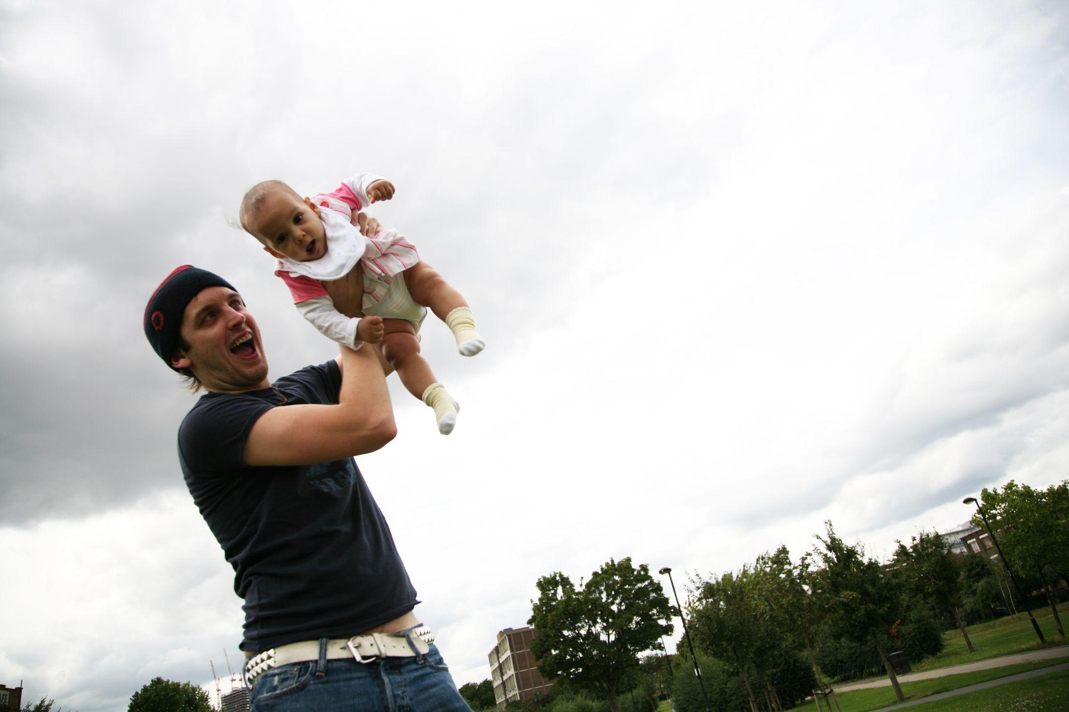 Un padre jugando sosteniendo a su bebé en un parque