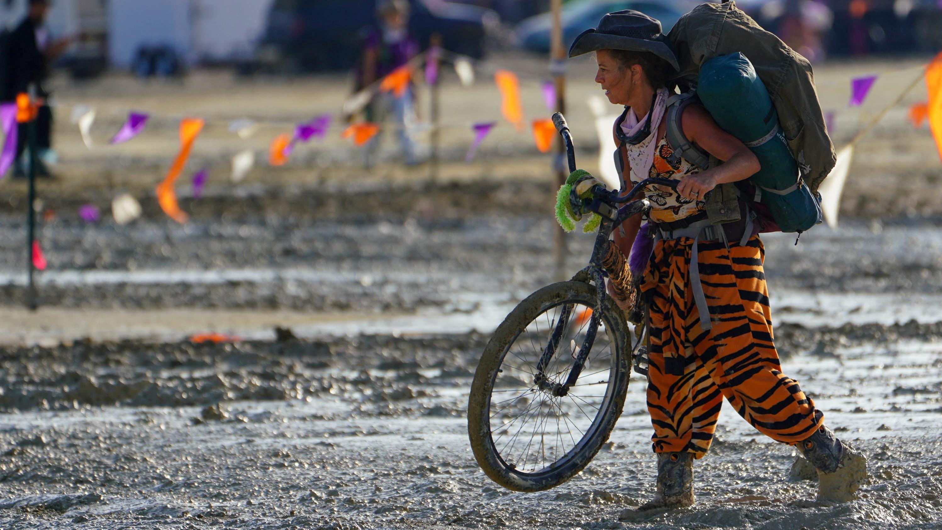Una participante de Burning Man camina con su bicicleta por el barro.