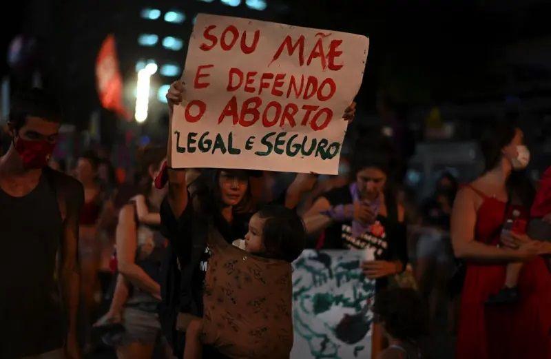 Protesto em defesa do aborto no Brasil, mulher segurando cartaz escrito: 'Sou mãe e defendo o aborto legal e seguro'