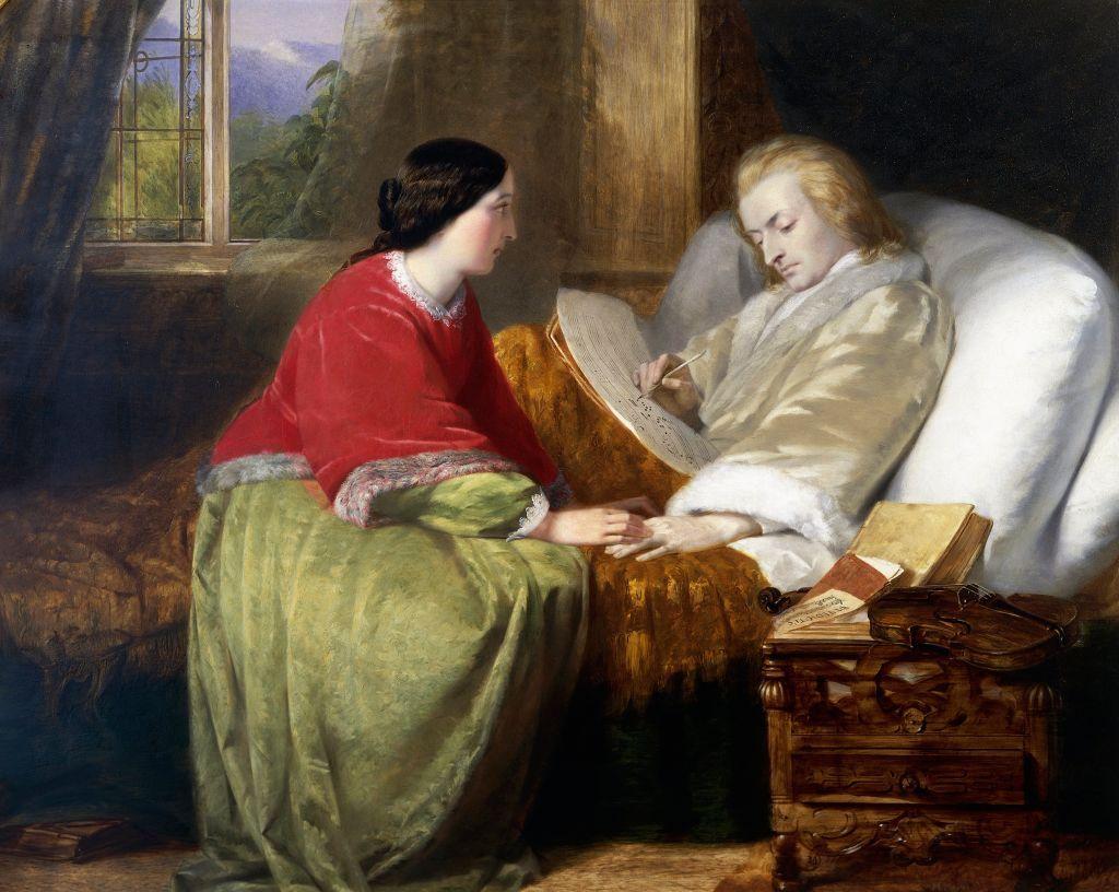 Mozart en cama escribiendo y su esposa sentada con él, tomándole la mano