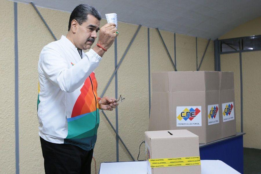 Maduro erguendo cédula de votação perto de urna