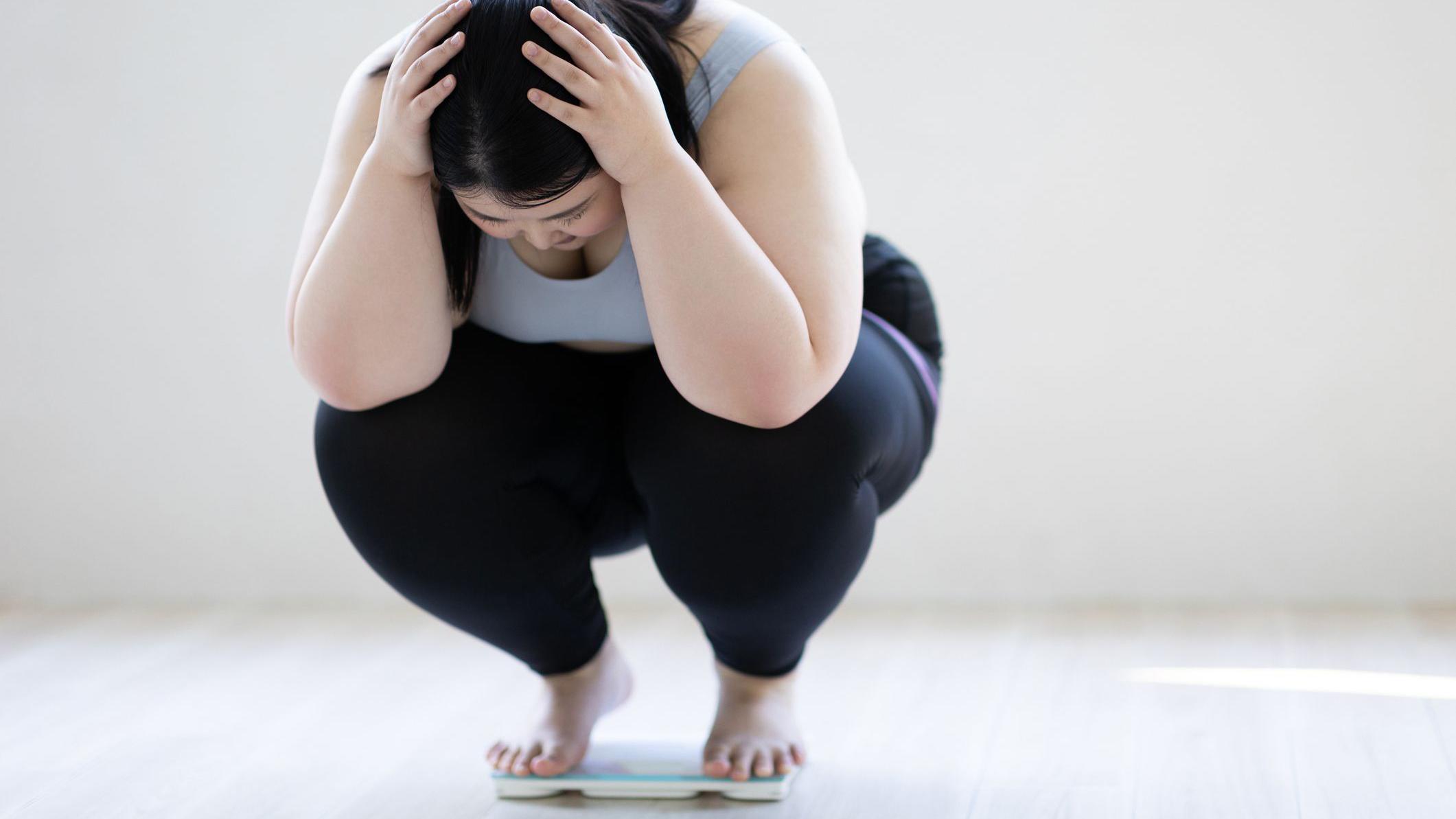 A woman squatting on a scale, frustrated. 