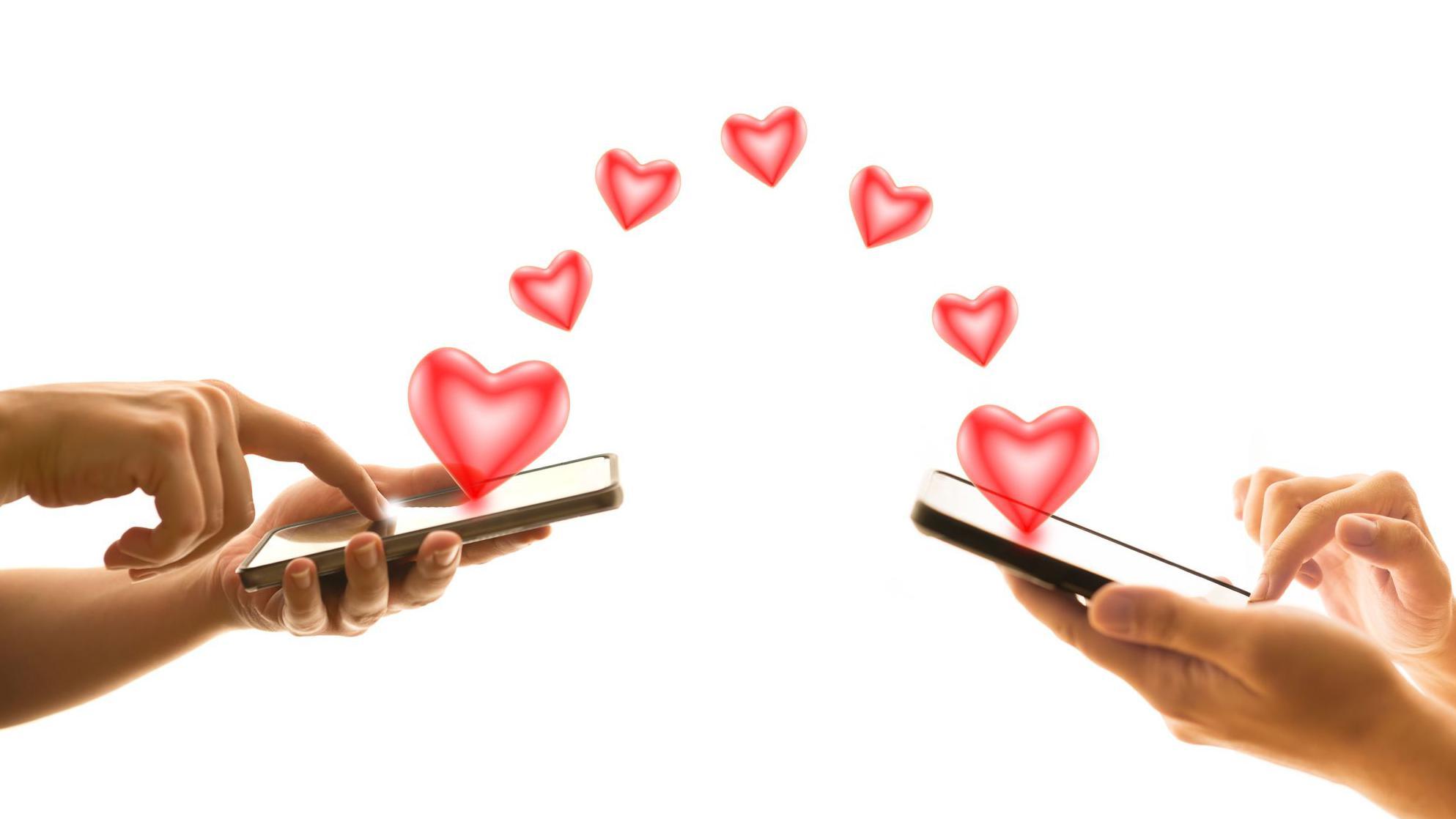 Las manos de dos personas comunicándose amorosamente con sus celulares, de donde salen unos corazones