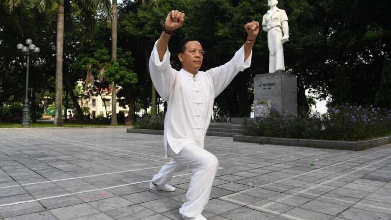 Fotografia mostra homem amarelo fazendo movimentos de artes marciais em uma praça