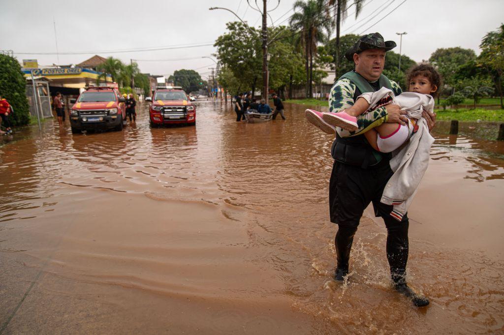 Criança sendo carregada no colo em meio à enchente