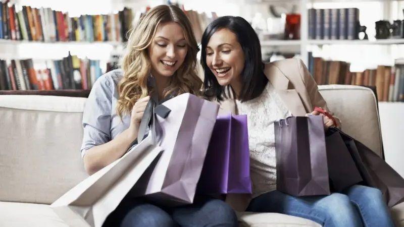 Foto de duas mulheres sentadas em um sofá com sacolas de compras 