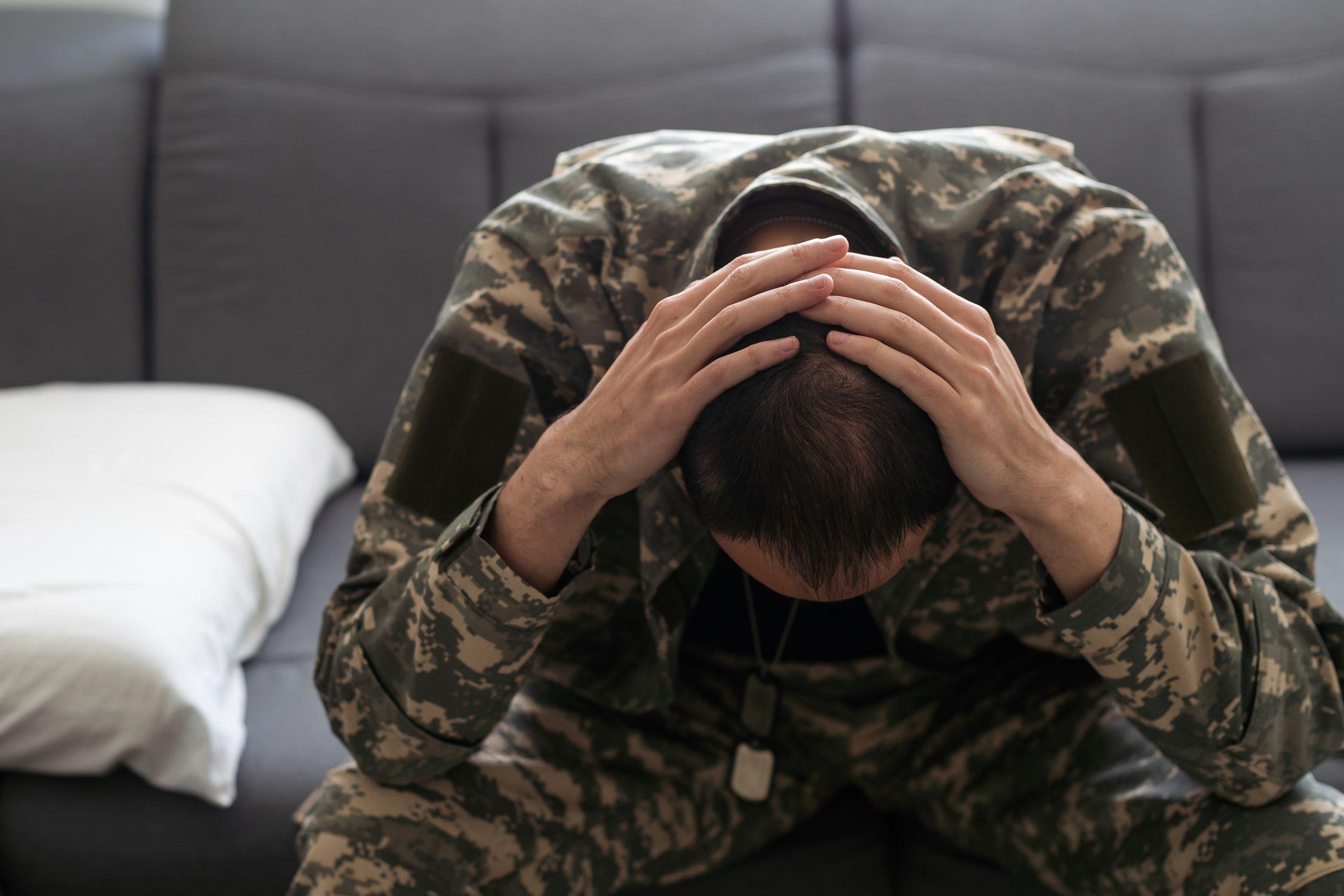 Homem fardado com roupas militares sentado, com as mãos na cabeça, demonstrando preocupação