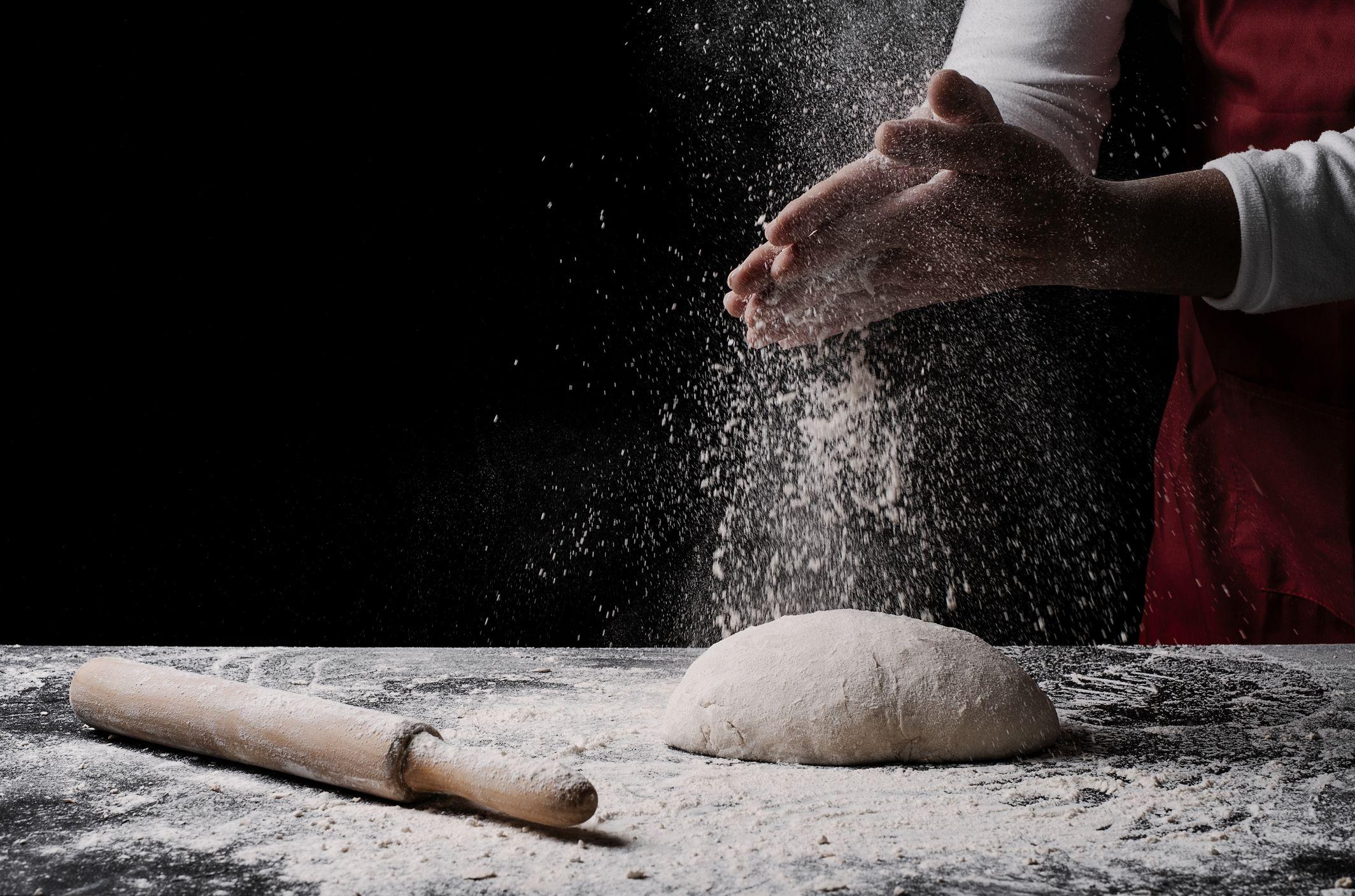 Mão de padeiro preparando massa de pão com farinha