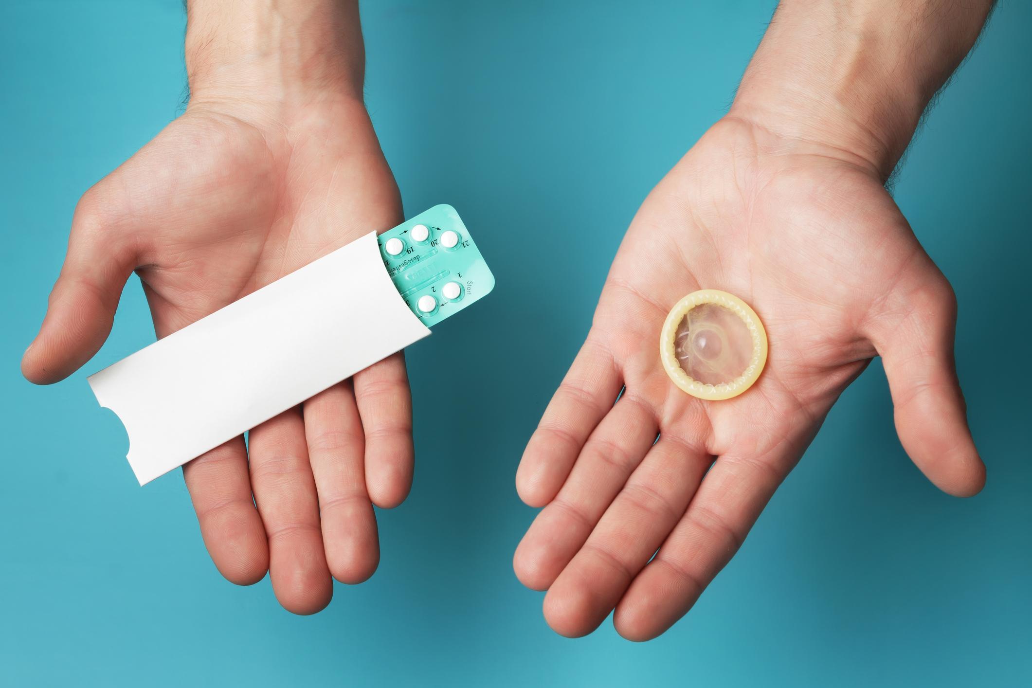 Duas mãos, uma mostrando uma cartela de pílula anticoncepcional, e a outra, uma camisinha
