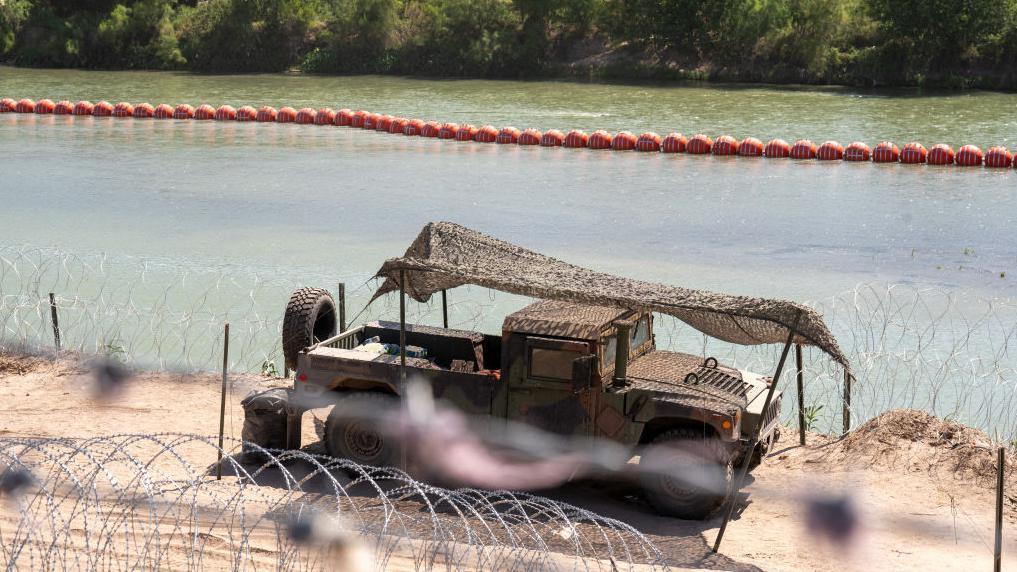 Un camión conduce frente a las boyas desplegadas en el río Bravo
