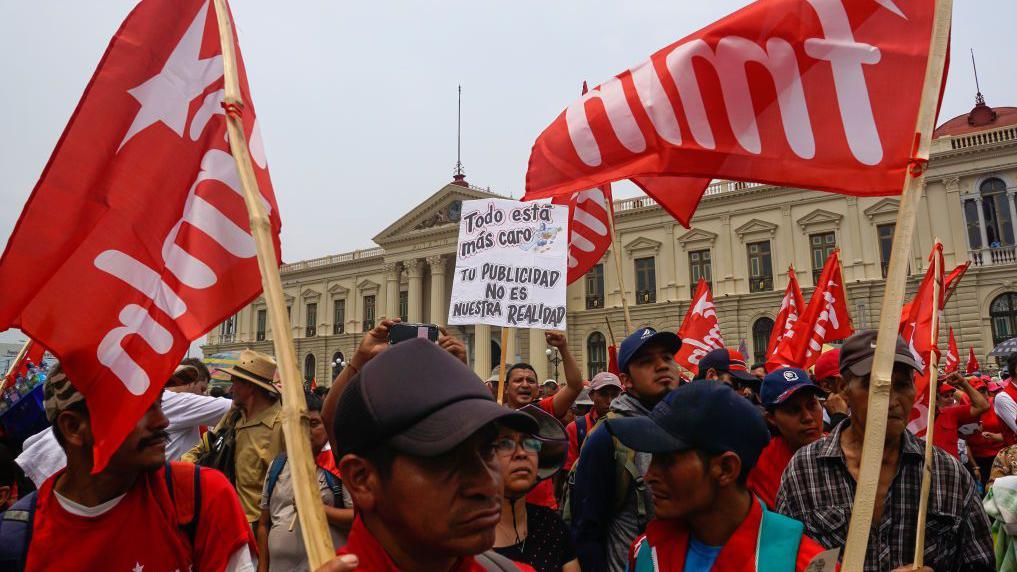 Simpatizantes del FMLN con banderas del partido y un cartel alusivo a la situación económica del país durante una manifestación del Día del Trabajador, el 1 de mayo de 2023, en San Salvador, El Salvador.