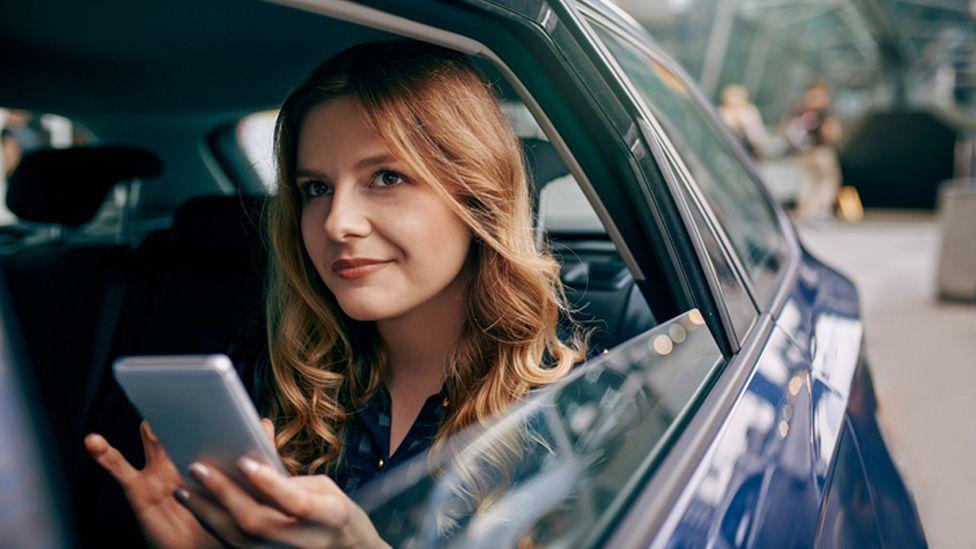 žena u automobilu drži telefon u ruci