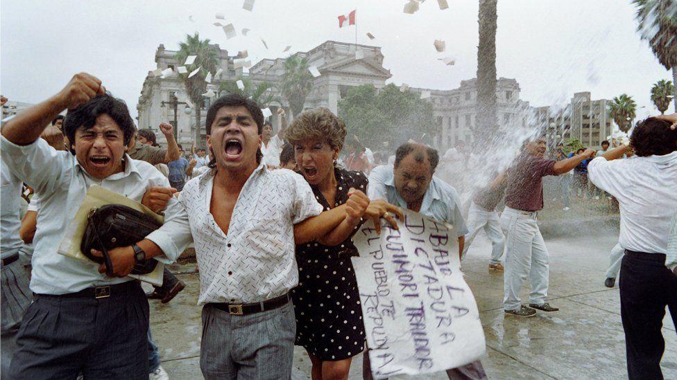 Manifestantes gritando; atrás, um jato de água 