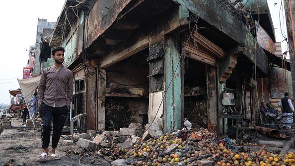 A man walks besides a burnt fruit shop after a parking space was set on fire by a mob during riots in Chandbagh area of New Delhi, India on 29 February 2020.