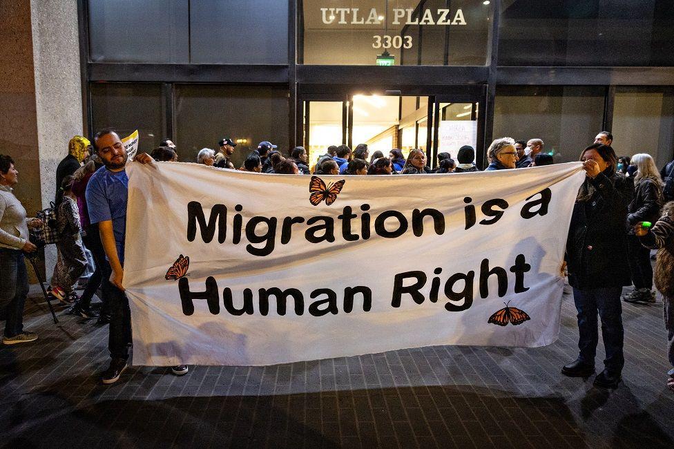 Dos personas con una pancarta que dice: "La inmigración es un derecho humano"