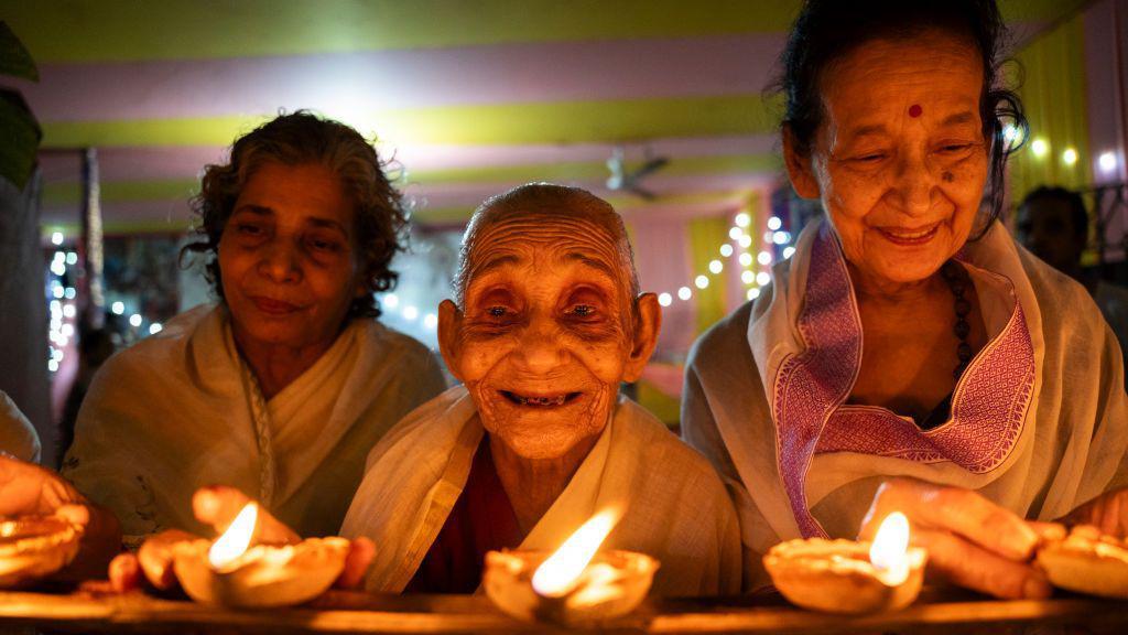 Mulheres idosas diante de lâmpadas acesas celebrando o Diwali, em Guwahati, Índia, em 1º de novembro de 2024