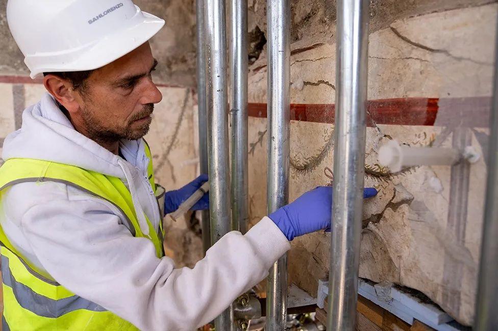 Um homem injeta uma cola de gesso por trás de um afresco