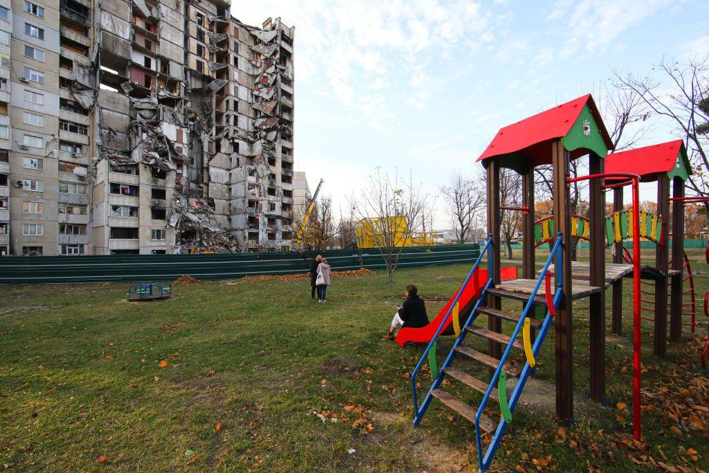 Niños ucranianos en un parque frente a un edificio derruido
