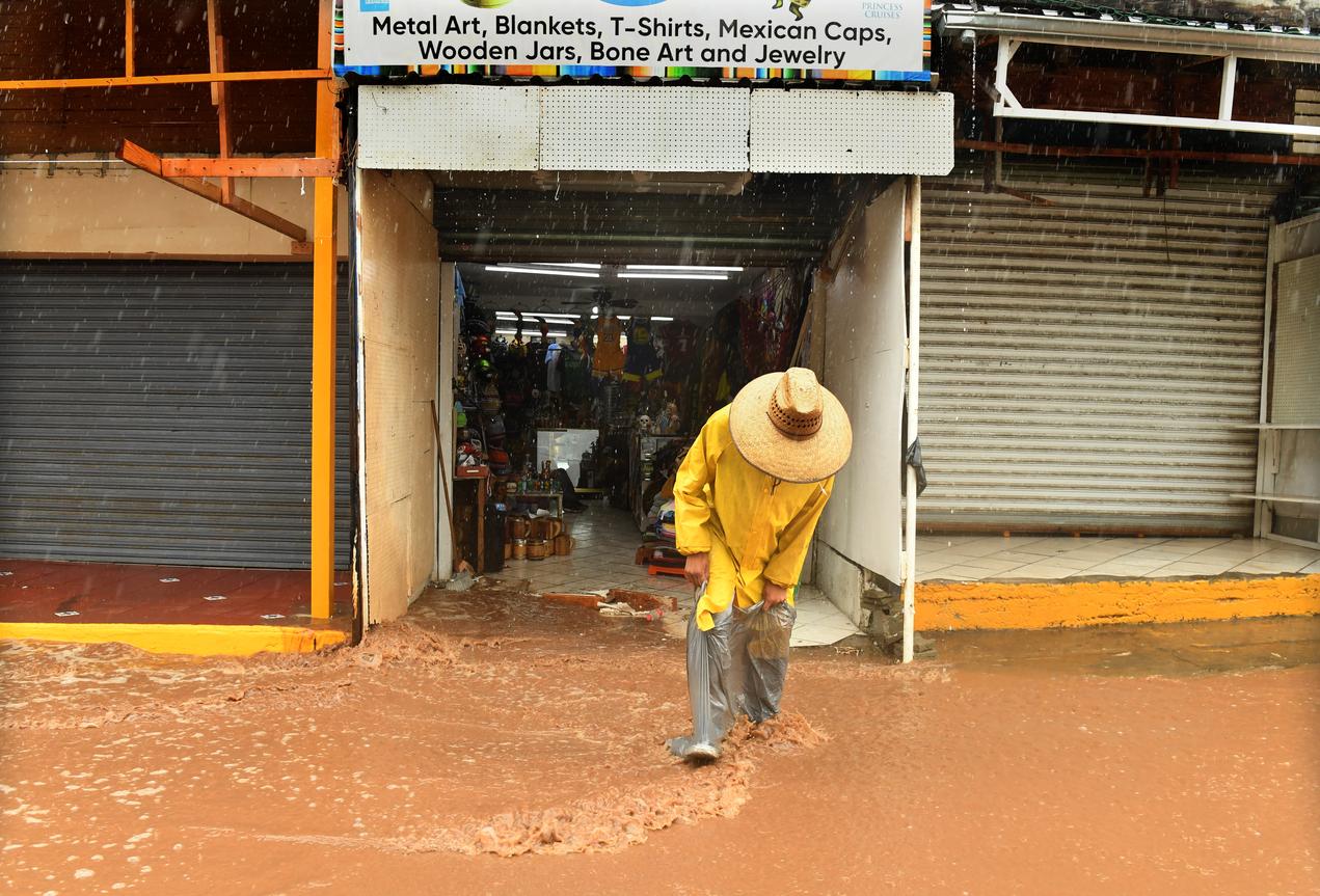 Un empleado sale de una tienda usando una bolsa de plástico para proteger sus zapatos del agua de la tormenta tropical Hilary en La Bufadora, México.