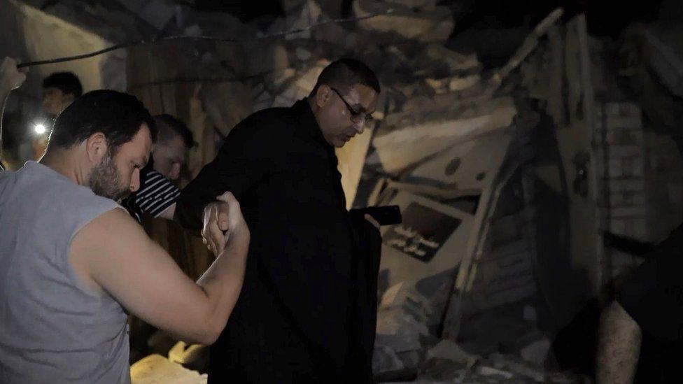 A rescuer holds a survivor's hand as he treads out of the rubble