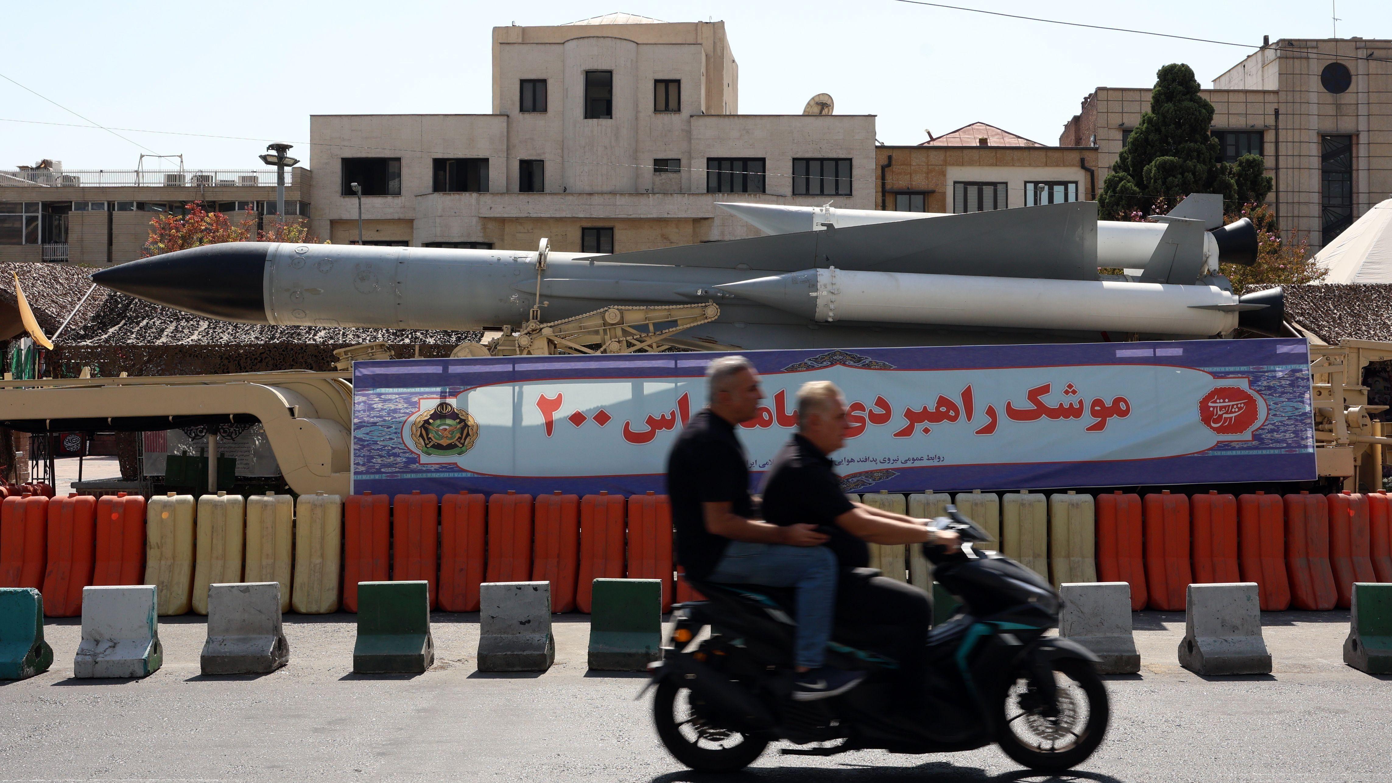 Dois iranianos passam de moto diante de um míssil em exibição na Praça Baharestan, em Teerã, Irã, durante a Semana da Defesa, em 24 de setembro.