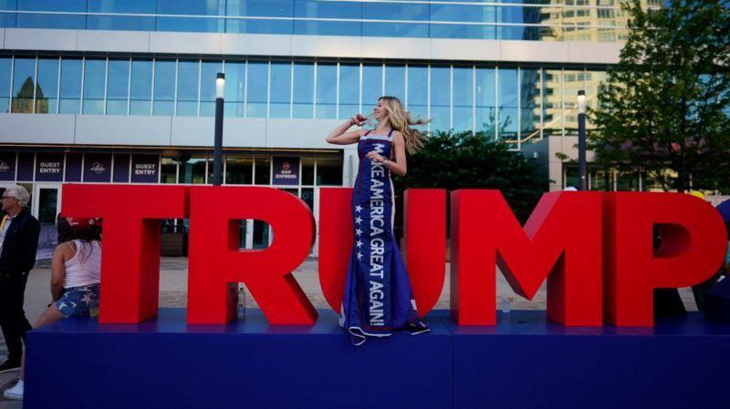 Mulher posa em frente a letreiro de Trump em evento político