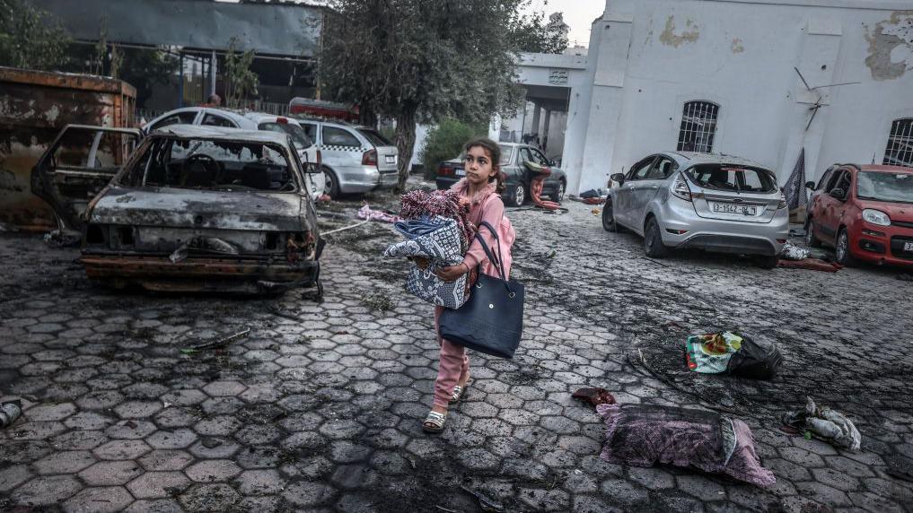 Una niña recolecta pertenencias cerca del hospital que fue atacado en Gaza.