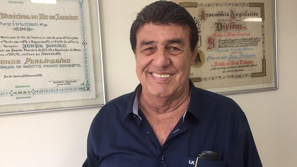 Jorge Perlingeiro sorrindo para foto em frente a certificados