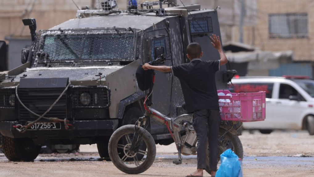 Un menor palestino frente a un vehículo del ejército israelí en Cisjordania.