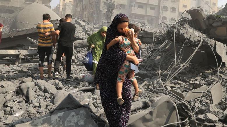 mujer lleva en brazos a un bebé entre los escombros en gaza 